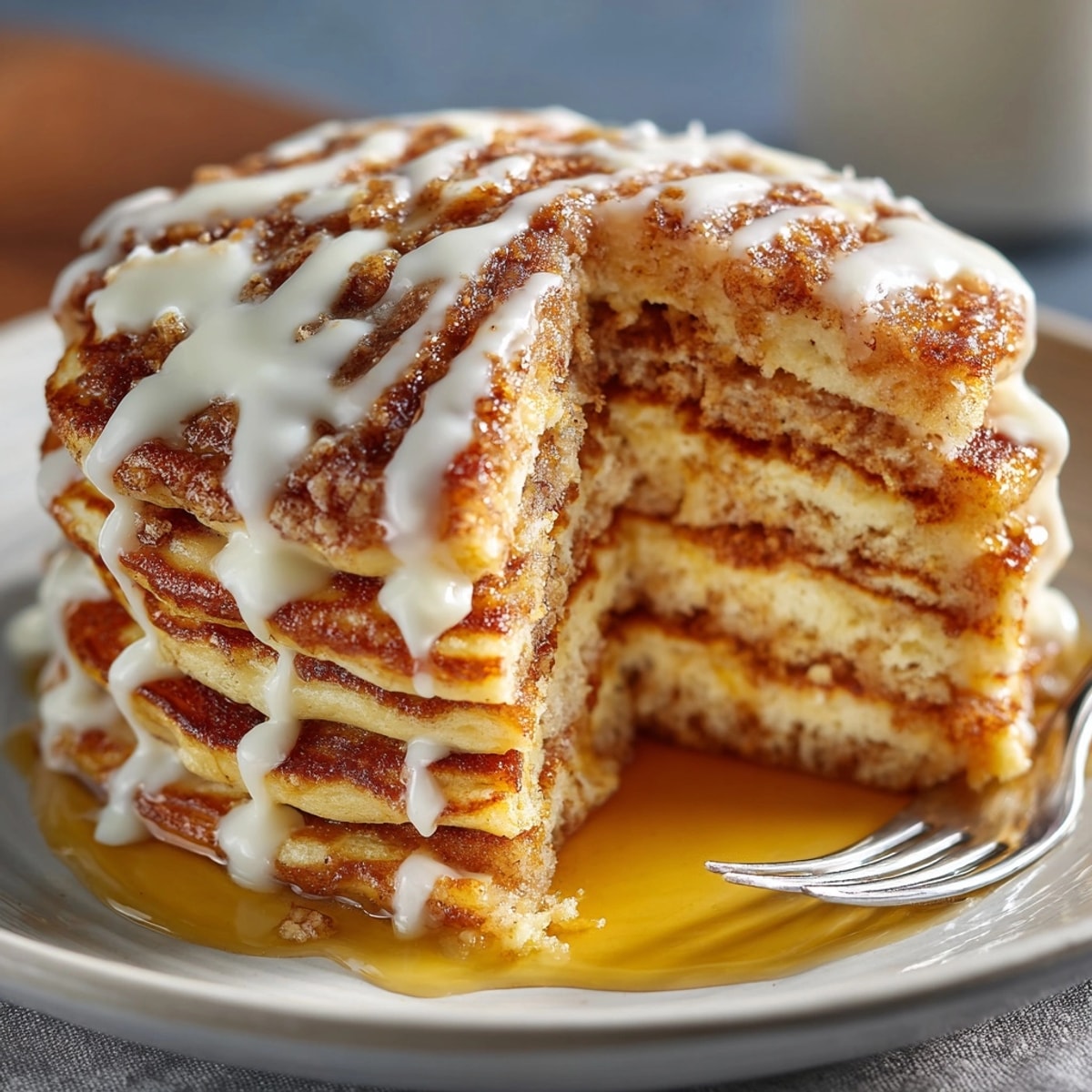 Golden brown cinnamon roll pancakes served warm, topped with luscious cream cheese glaze drizzle.