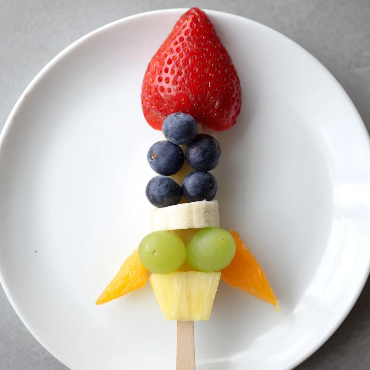 Vibrant Rocket Ship Fruit Skewers feature strawberries, grapes, and pineapple, a colorful snack for kids.