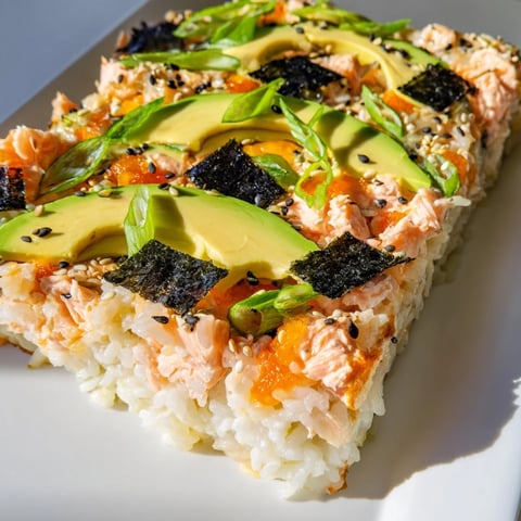 Warm, bubbly Sushi Bake Casserole, topped with avocado and sesame seeds, ready to serve with soy sauce.