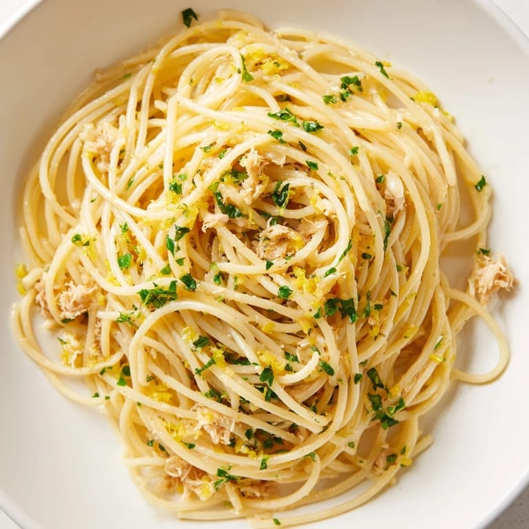 Delicious pasta with lemon-garlic tuna spaghetti, garnished with fresh parsley and lemon wedges for serving.