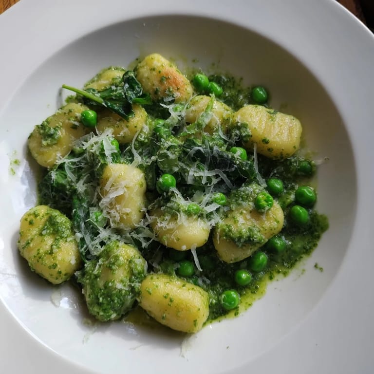 A rustic wooden table holds the finished Pesto Pea Gnocchi Skillet, garnished with lemon zest and a glass of white wine.