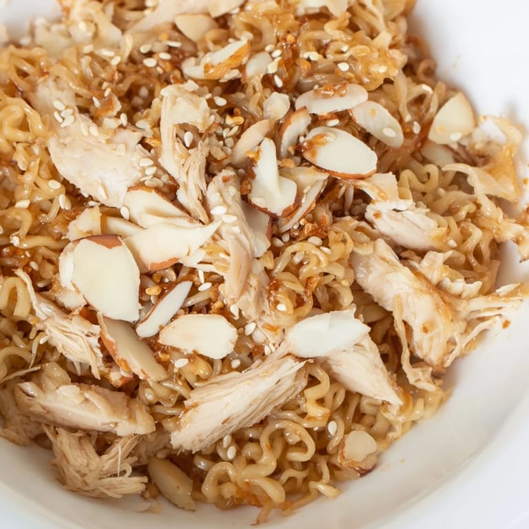 Golden ramen noodles and fresh cilantro garnish this refreshing Crunchy Ramen Chicken Salad, drizzled with a sweet sesame dressing in a white bowl.