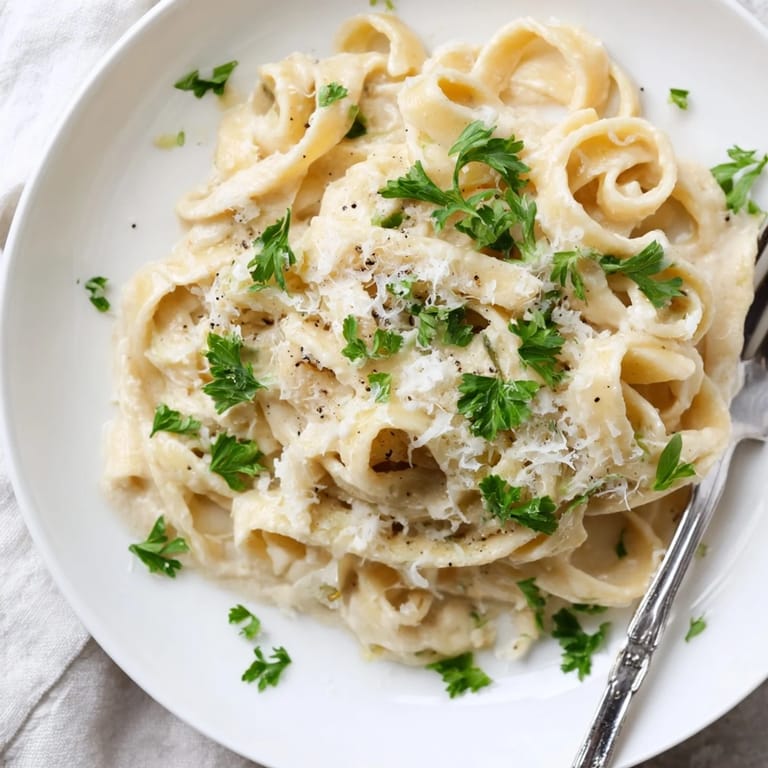 A bowl of Easy Creamy Cauliflower Alfredo features fettuccine coated in a velvety sauce, steaming gently.