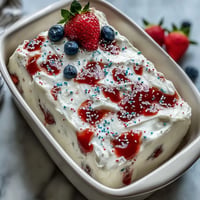 Festive red and blue gelatin swirls through white cake, topped with whipped topping and patriotic sprinkles for Memorial Day.  